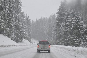 A vehicle drives along a snow-covered road in the mountains.