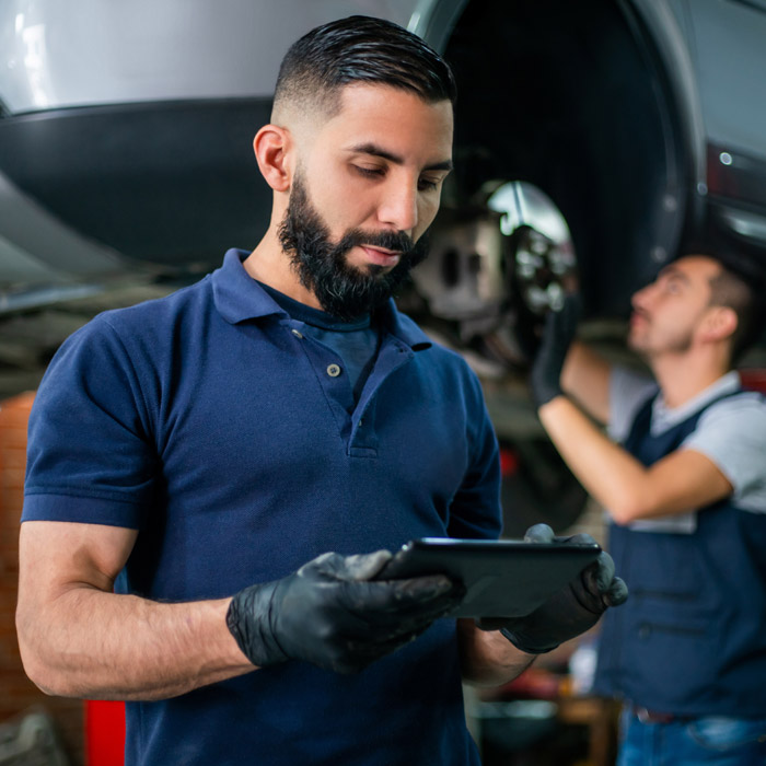 mechanic looking at ipad in front of car