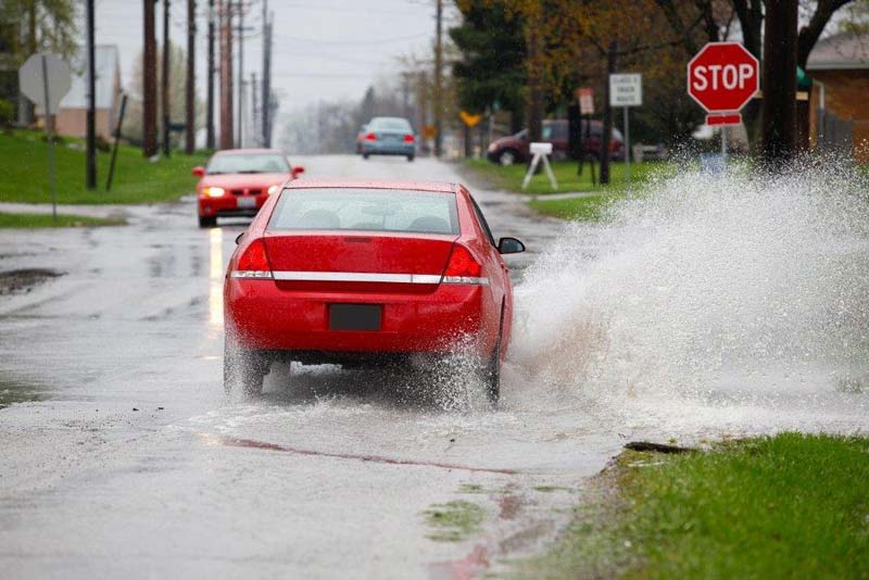 Red car driving through water on rainy street
