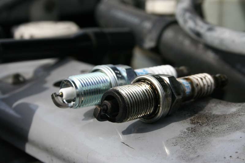 New and old spark plugs on engine surface